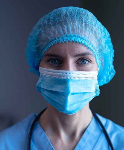 Portrait of caucasian female doctor in hospital wearing face mask, medical cap and scrubs. medical professional at work during coronavirus covid 19 pandemic.